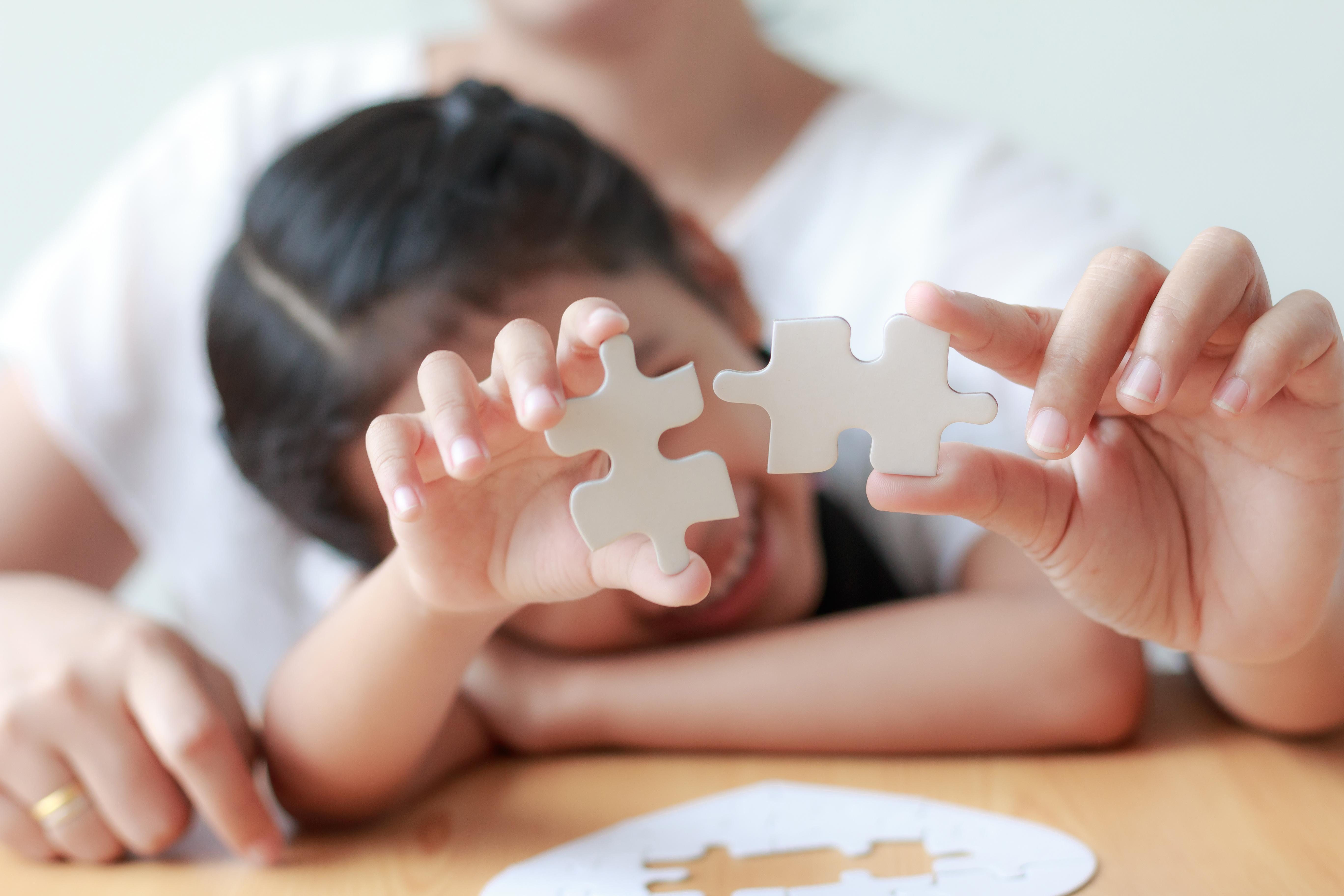 Asian little girl playing jigsaw puzzle with her mother for family concept shallow depth of field select focus on hands Asian little girl playing jigsaw puzzle with her mother for family concept shallow depth of field select focus on hands